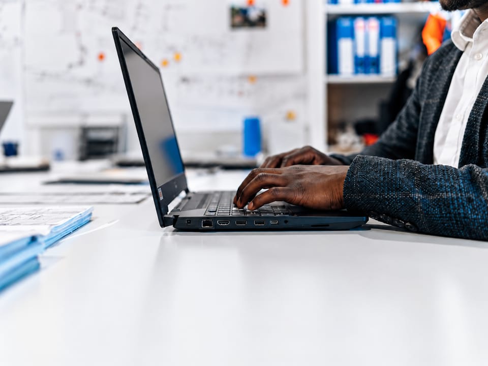 Close-up of hands typing on a laptop at a desk in a bright office.